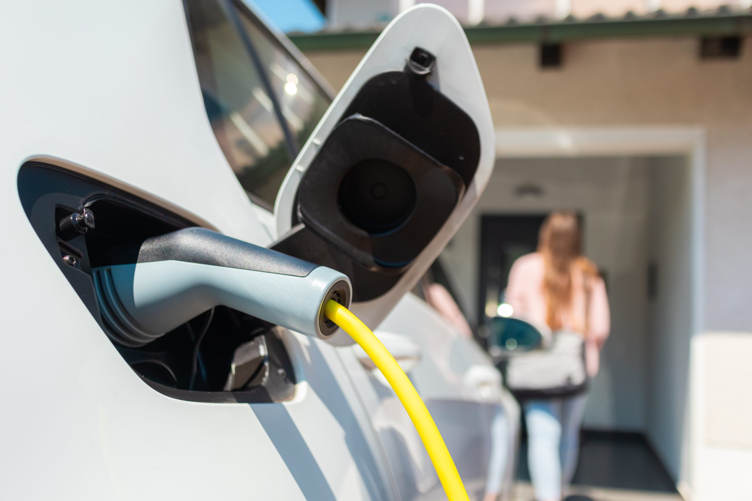 Vrouw laadt elektrische auto thuis op met kabel.