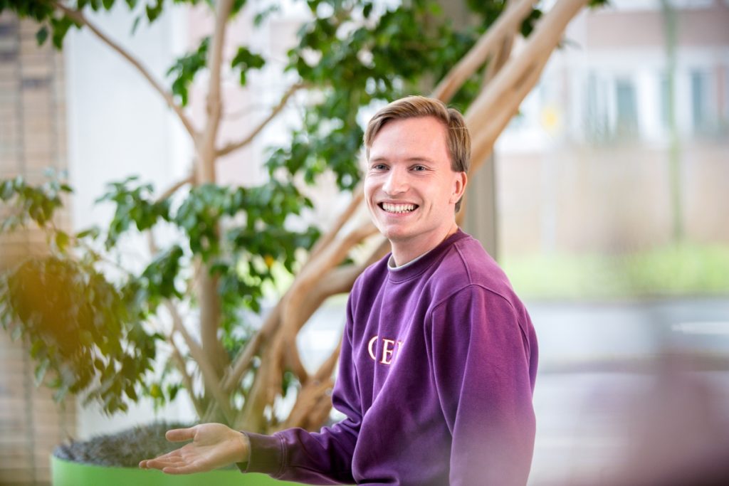 Een software engineer met een paarse trui zit in de centrale hal bij Technolution, portret 2 van 5