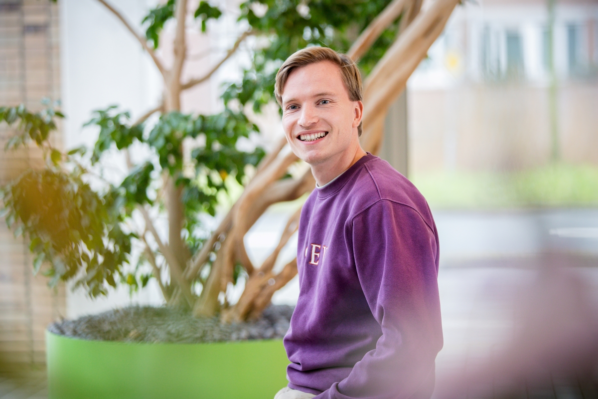 Een software engineer met een paarse trui zit in de centrale hal bij Technolution, portret 3 van 5